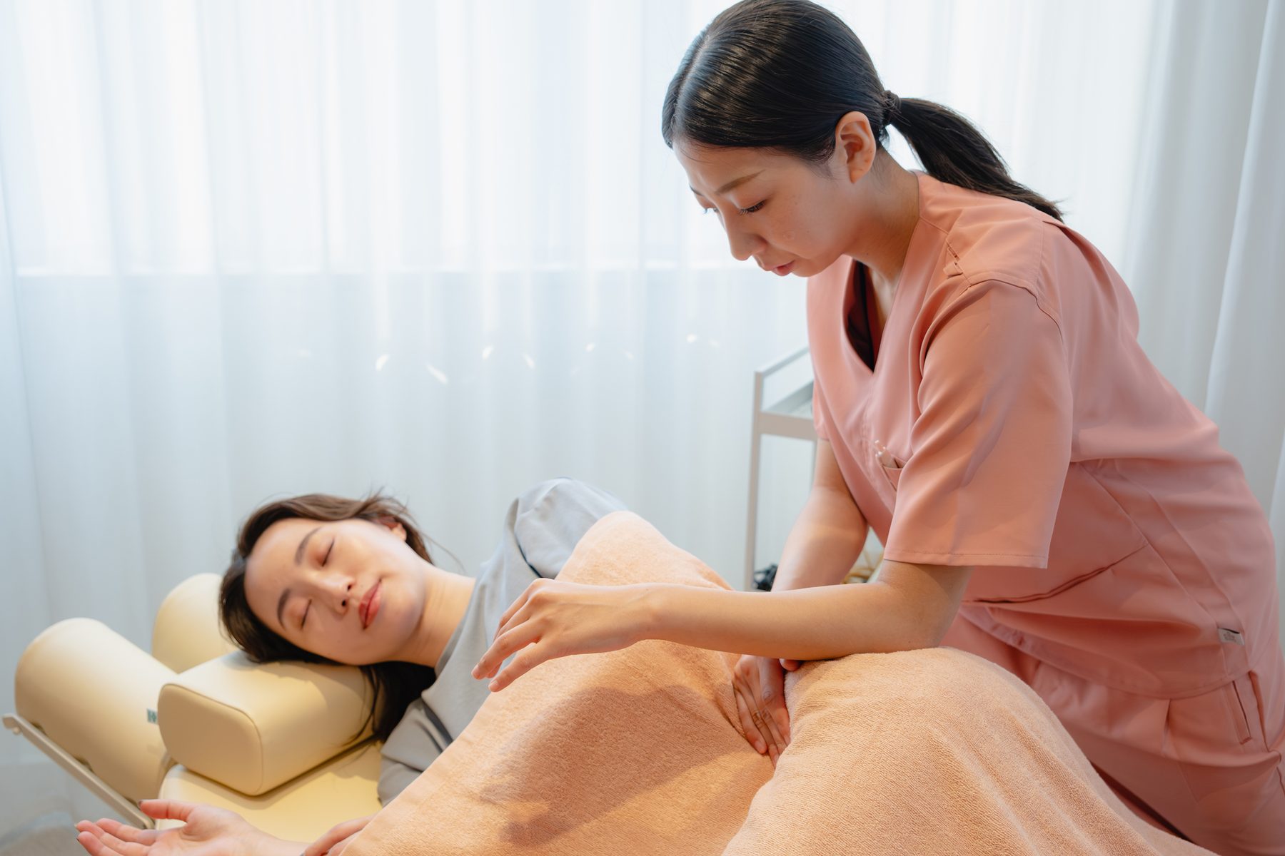 横になった患者様の胸元に手を当て、筋膜のすべりを確かめる女性のセラピスト